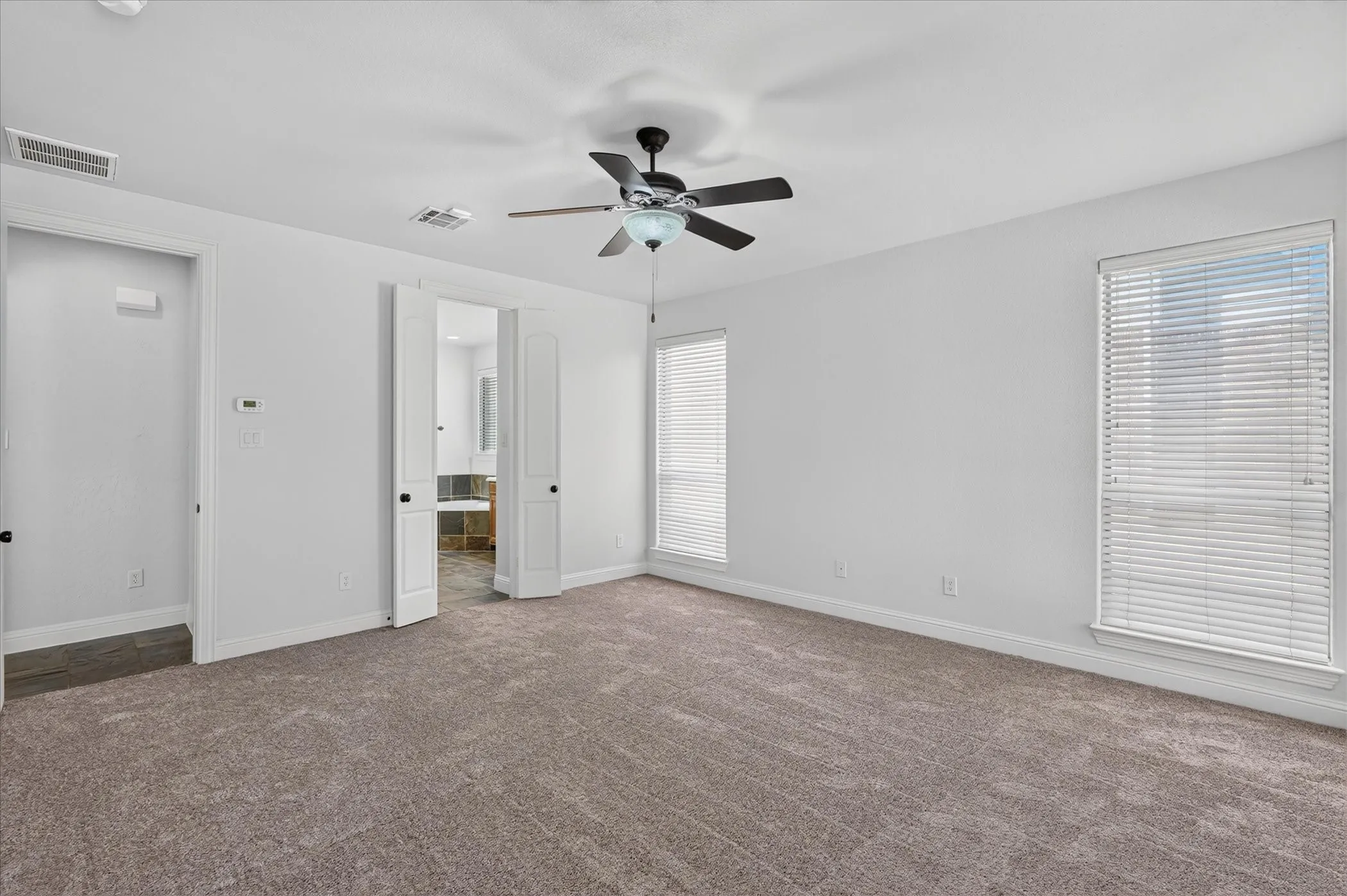 Carpeted room with white walls, two windows with blinds, a ceiling fan, and two interior doors