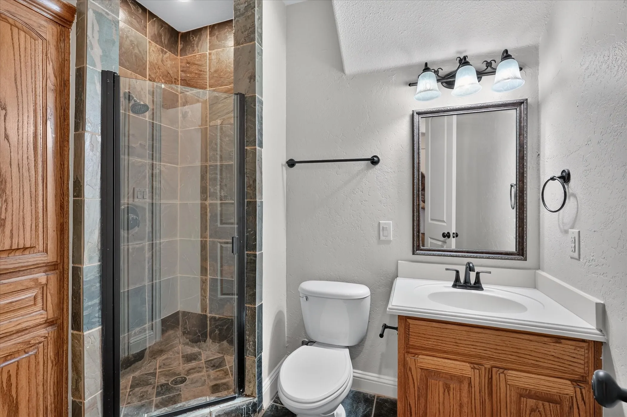 Tiled shower enclosure with a glass door, wood vanity with an integrated sink, and an ornamental framed mirror