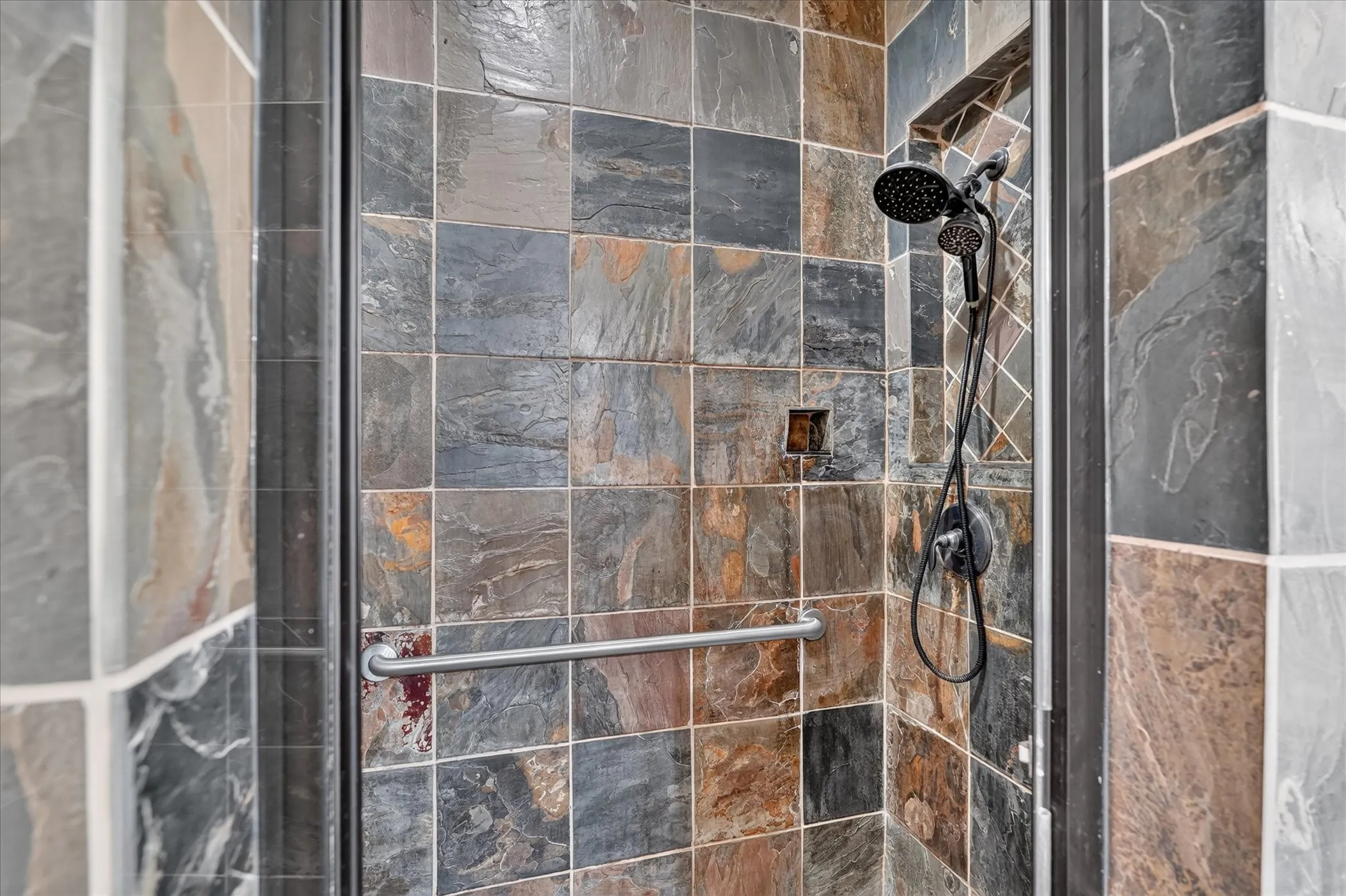 Glass-enclosed shower with slate-tiled walls, a built-in shower niche, and a matte black dual shower head system