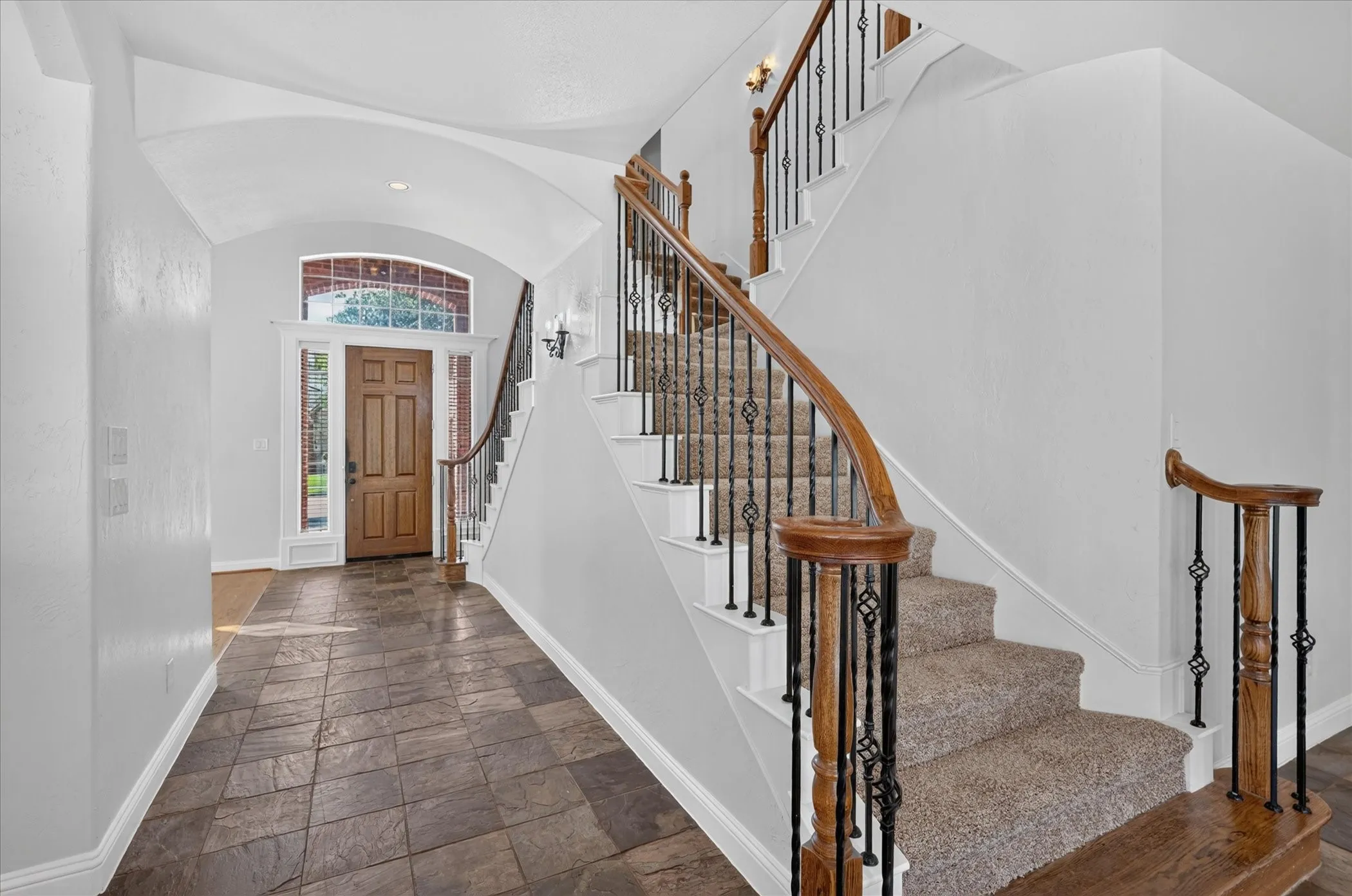 Archway entry with a wooden door, sidelight windows, and an arched transom window