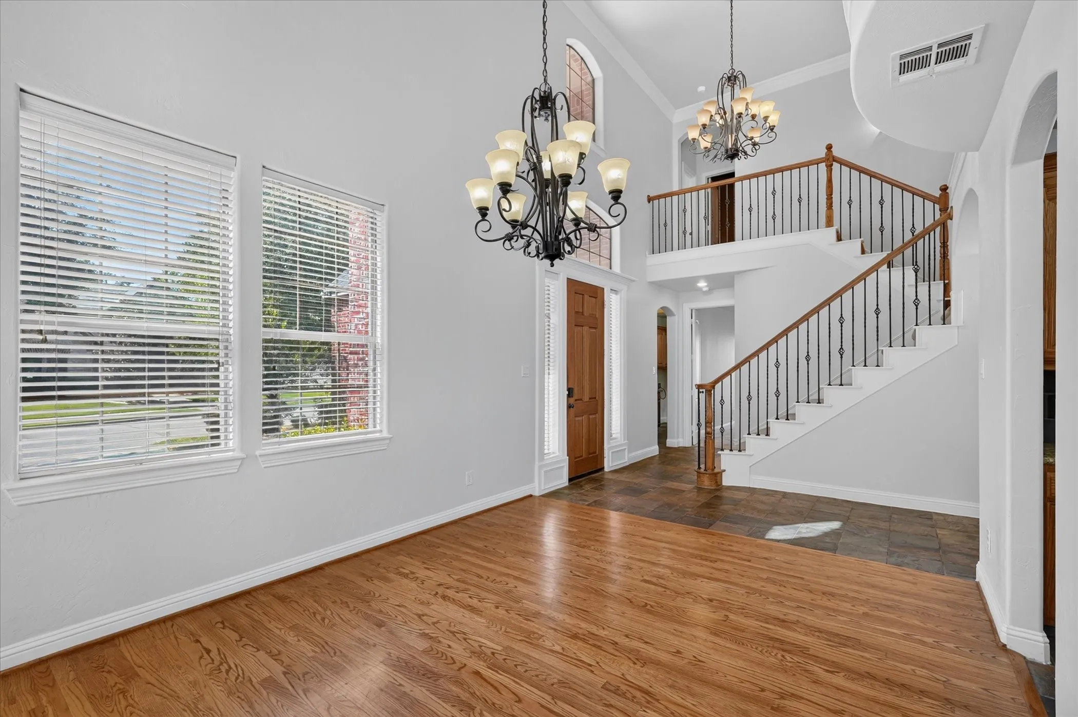 Two-story entryway featuring high ceilings, wood-finish flooring, and a grand staircase with wrought iron balusters