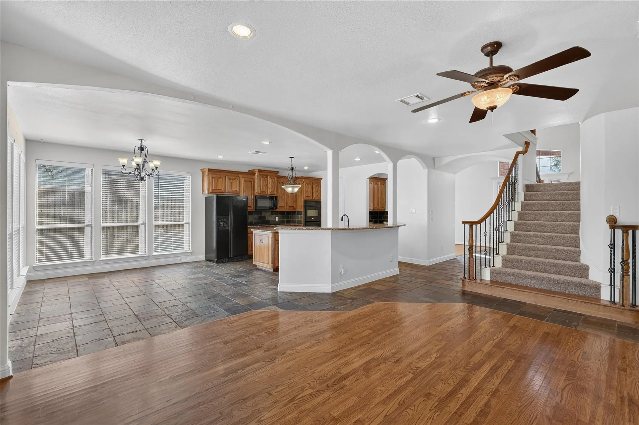 Hardwood flooring, kitchen with wood cabinetry, arched doorways, carpeted staircase with wrought iron balusters, and recessed lighting