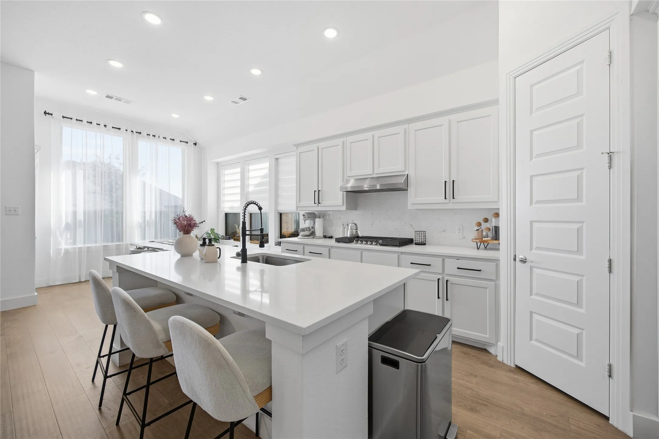 Spacious kitchen featuring an expansive island, white cabinetry, integrated sink with a black matte faucet, stainless steel appliances, and light wood-finish flooring