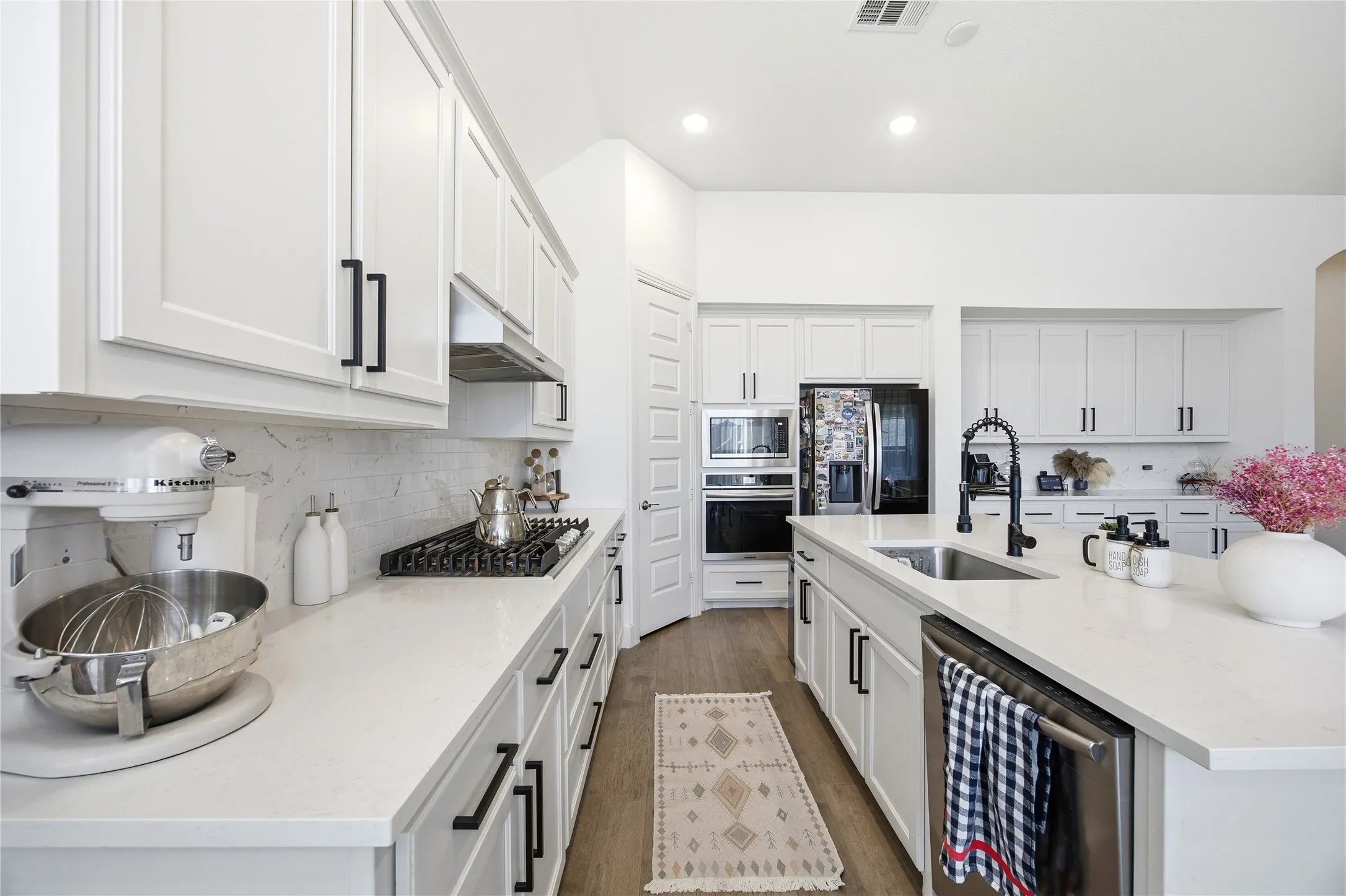 White shaker cabinetry with matte black hardware, integrated stainless steel appliances, light-toned countertops, and wood-finish flooring