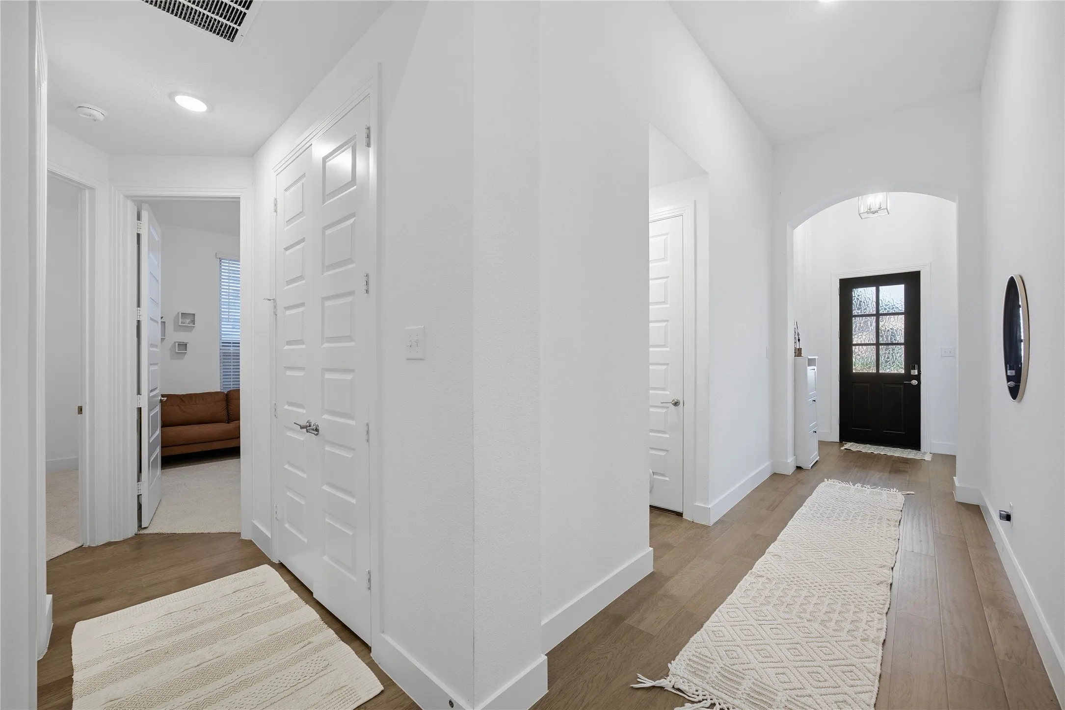 Wood-finish flooring throughout, bright white walls, recessed lighting, arched entryway, and a dark-paneled front door with frosted glass