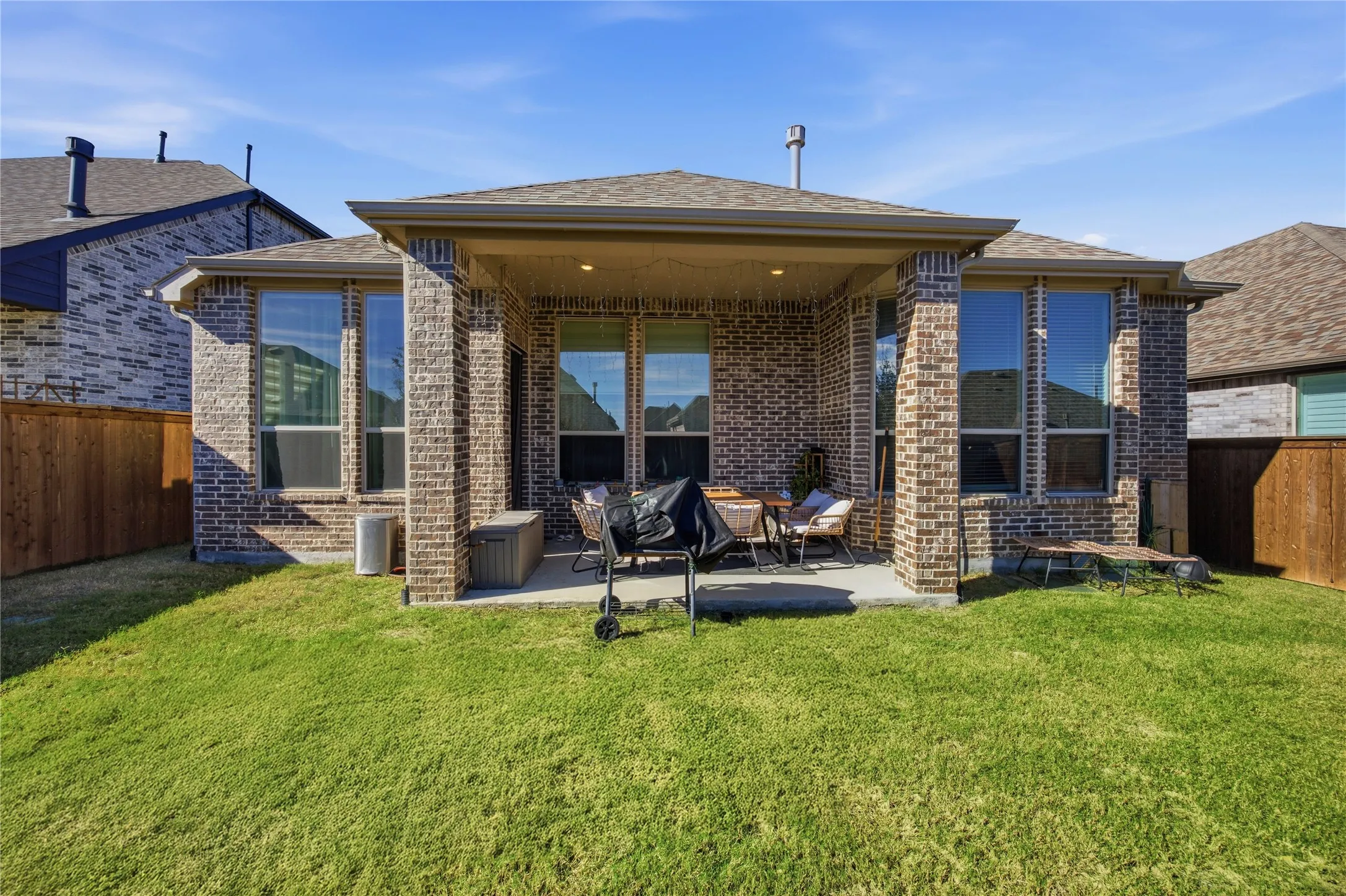 Brick exterior with a covered patio, expansive lawn, and privacy fencing