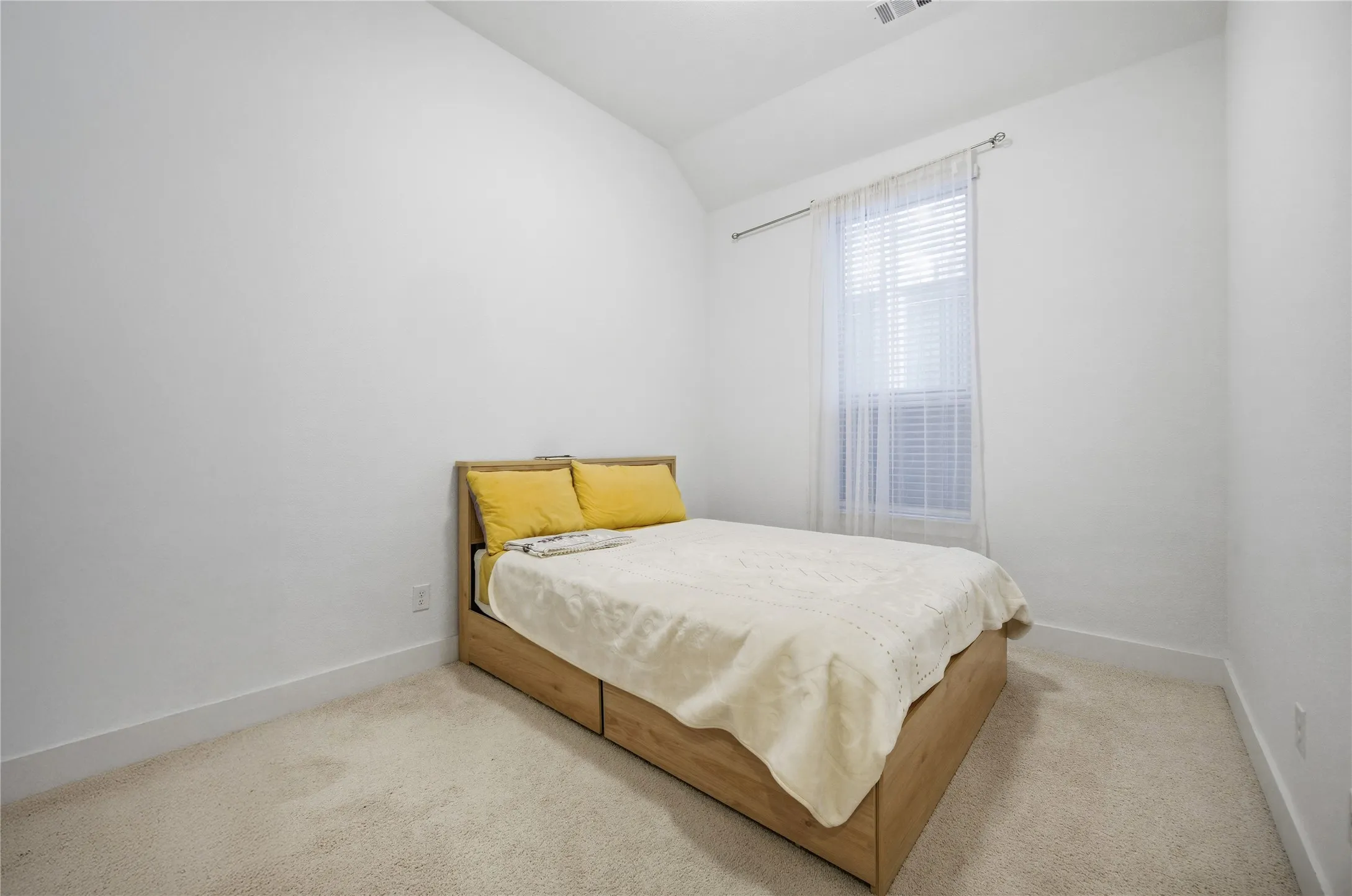 Neutral tone wall paint, light-colored carpeting, a single window with blinds, and a ceiling-mounted light fixture