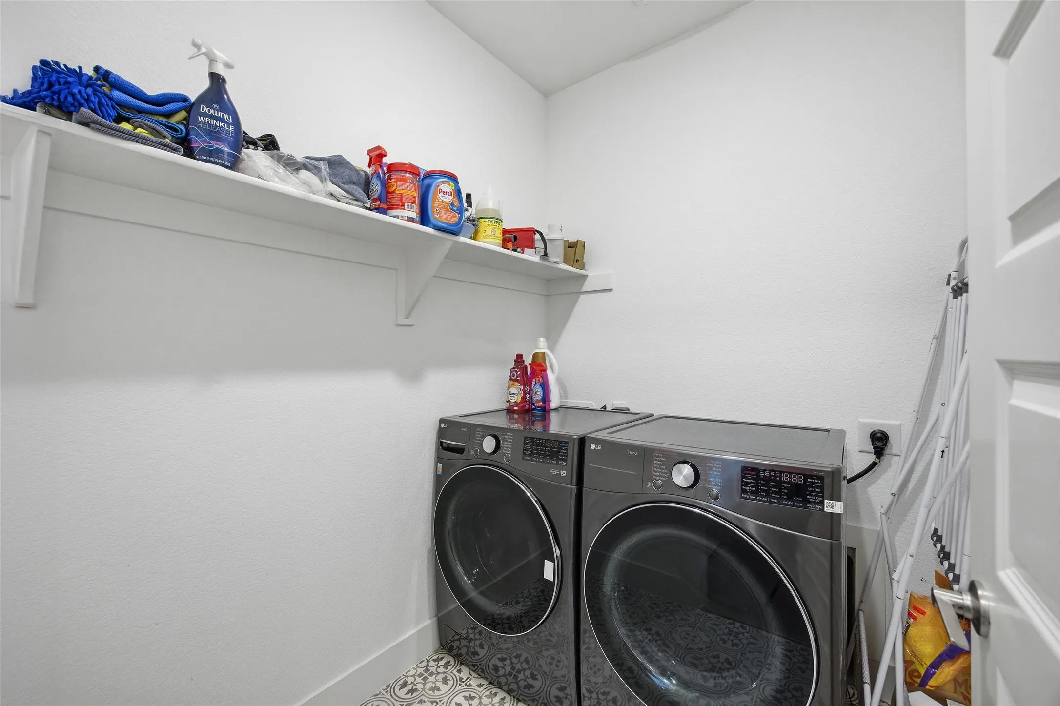 Dedicated laundry area with patterned floor tiles and an overhead storage shelf