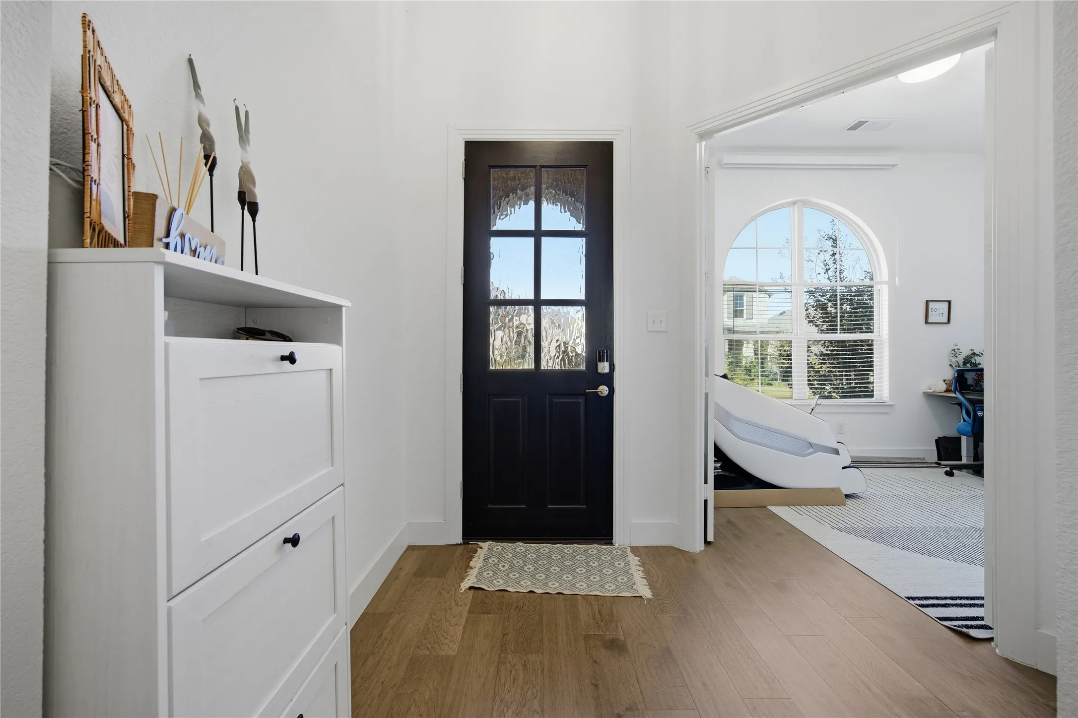 Wood-finish flooring, white walls, and a black front door with decorative glass panels