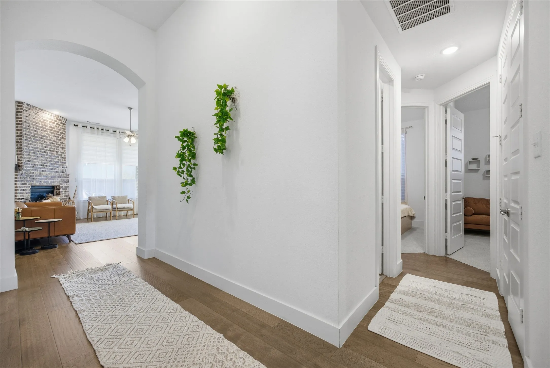 Arched entryway leading to a living area with a brick fireplace, wood-finish flooring, and white interior doors