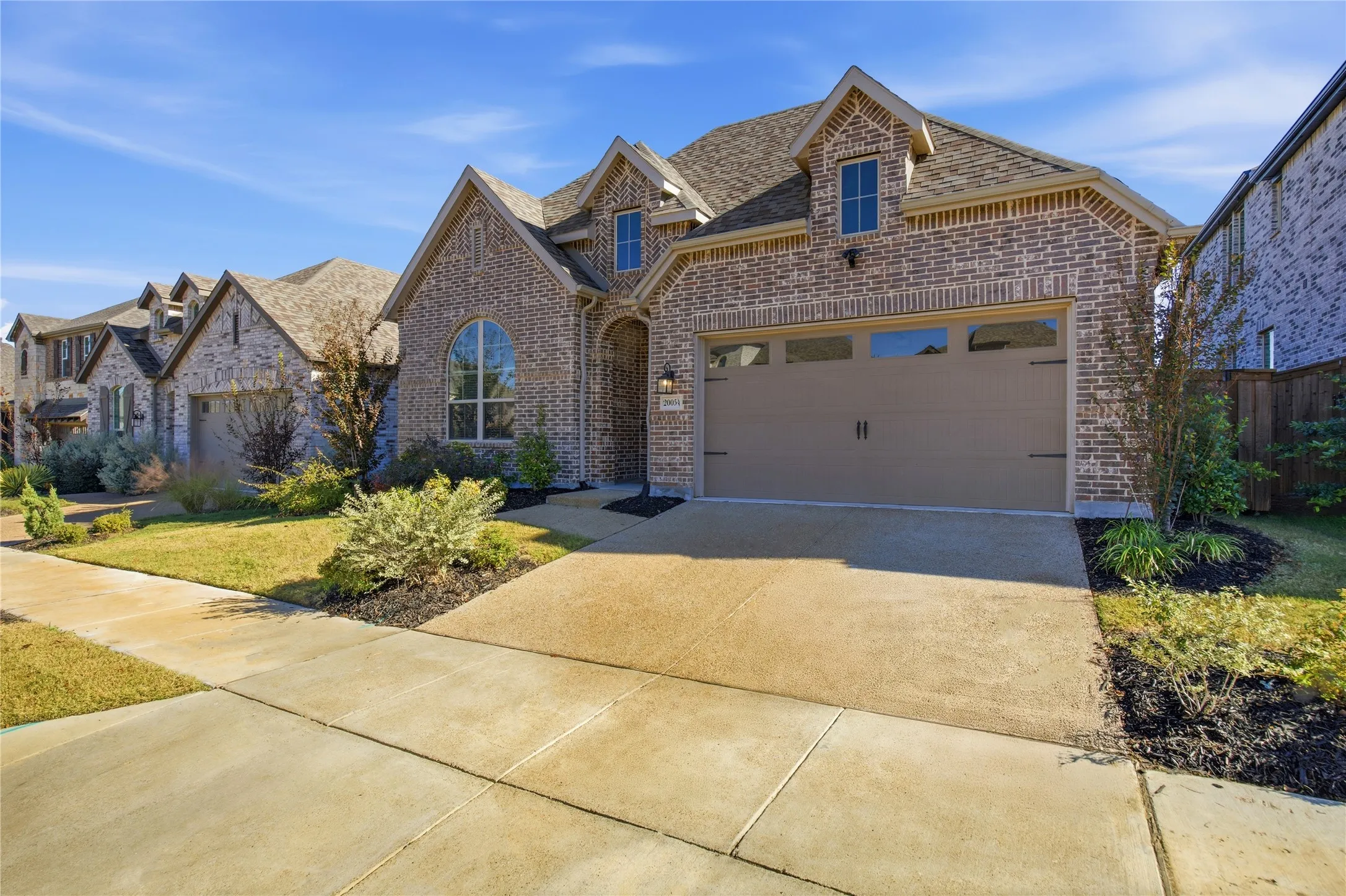 Brick exterior with gabled roof lines, featuring an arched window, an attached two-car garage, and established landscaping