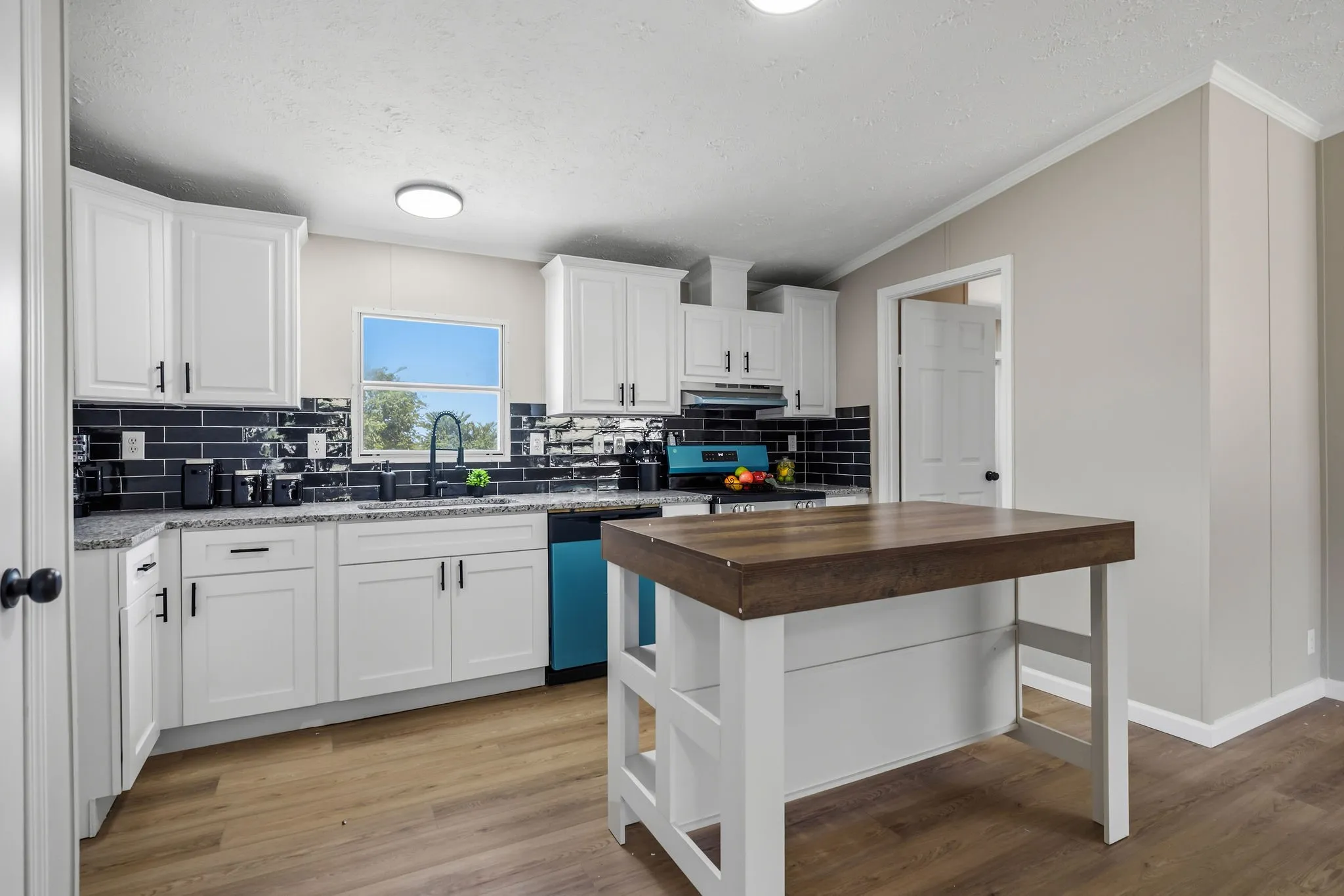 Kitchen featuring white cabinetry, dark subway tile backsplash, light-toned countertops, wood-finish flooring, and a central island with a wood-finish top