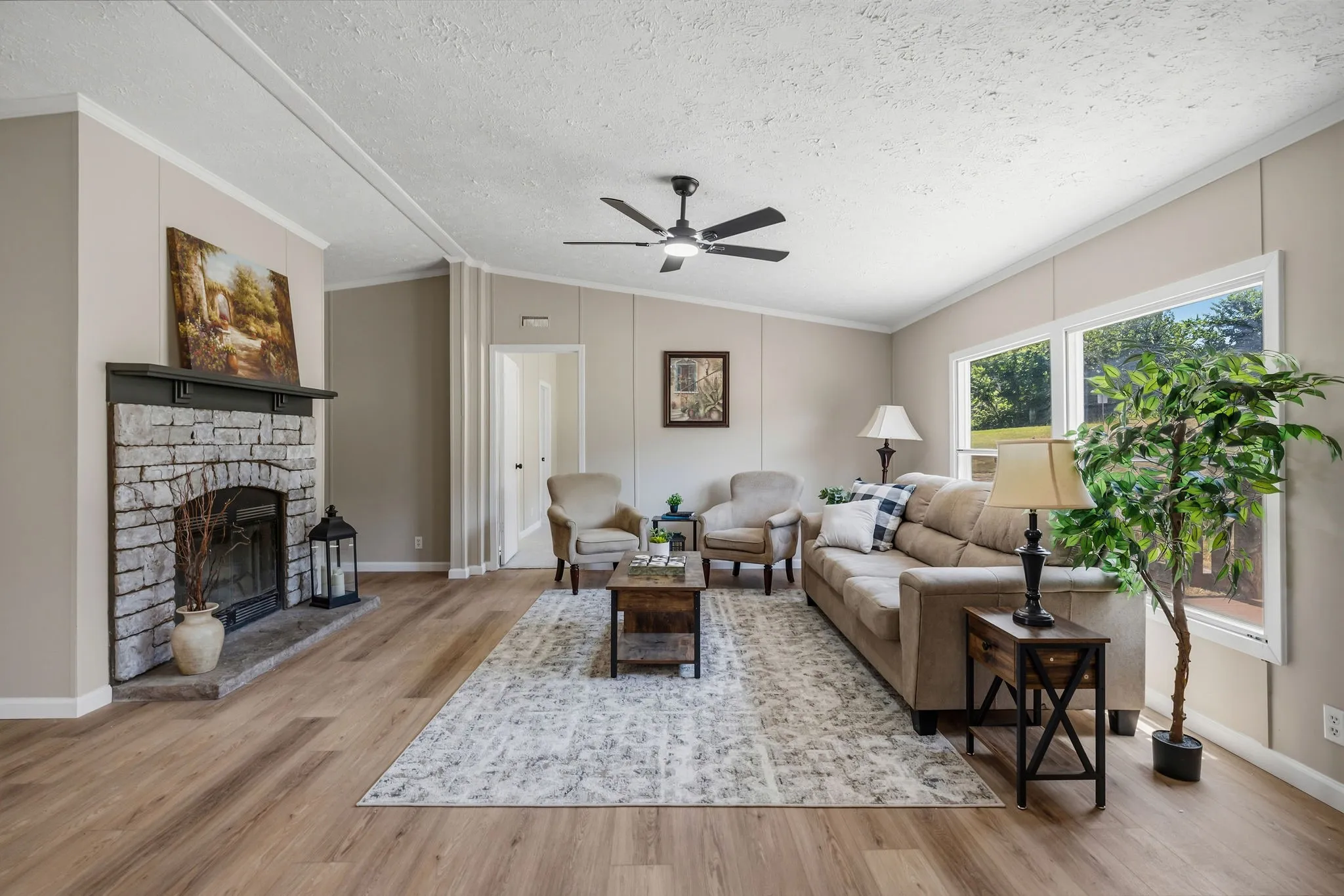 Spacious living area featuring wood-finish flooring, a stone-faced fireplace with a dark wood mantel, and a ceiling fan