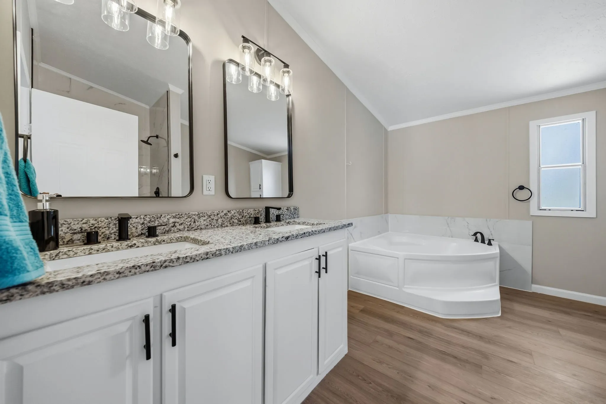 Dual vanity with granite countertops, white cabinetry, matte black fixtures, built-in corner soaking tub, and wood-finish flooring