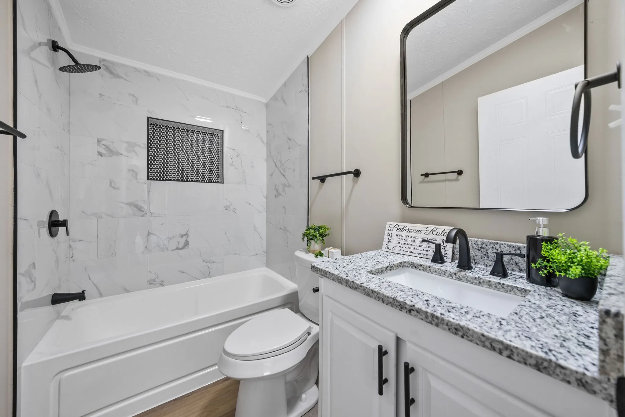 White tile surround with recessed niche, integrated bathtub, black-finish shower fixtures, vanity with undermount sink, and granite countertop