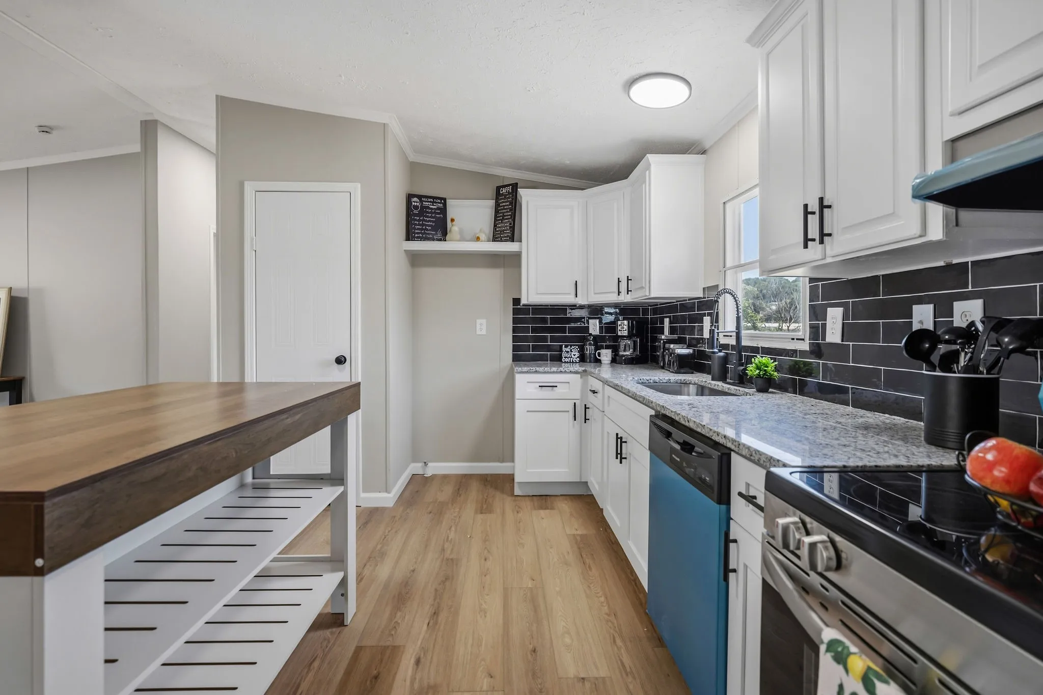 Kitchen featuring a wood-top island with open shelving, wood-finish flooring, white cabinetry with black hardware, black subway tile backsplash, and light-toned countertops