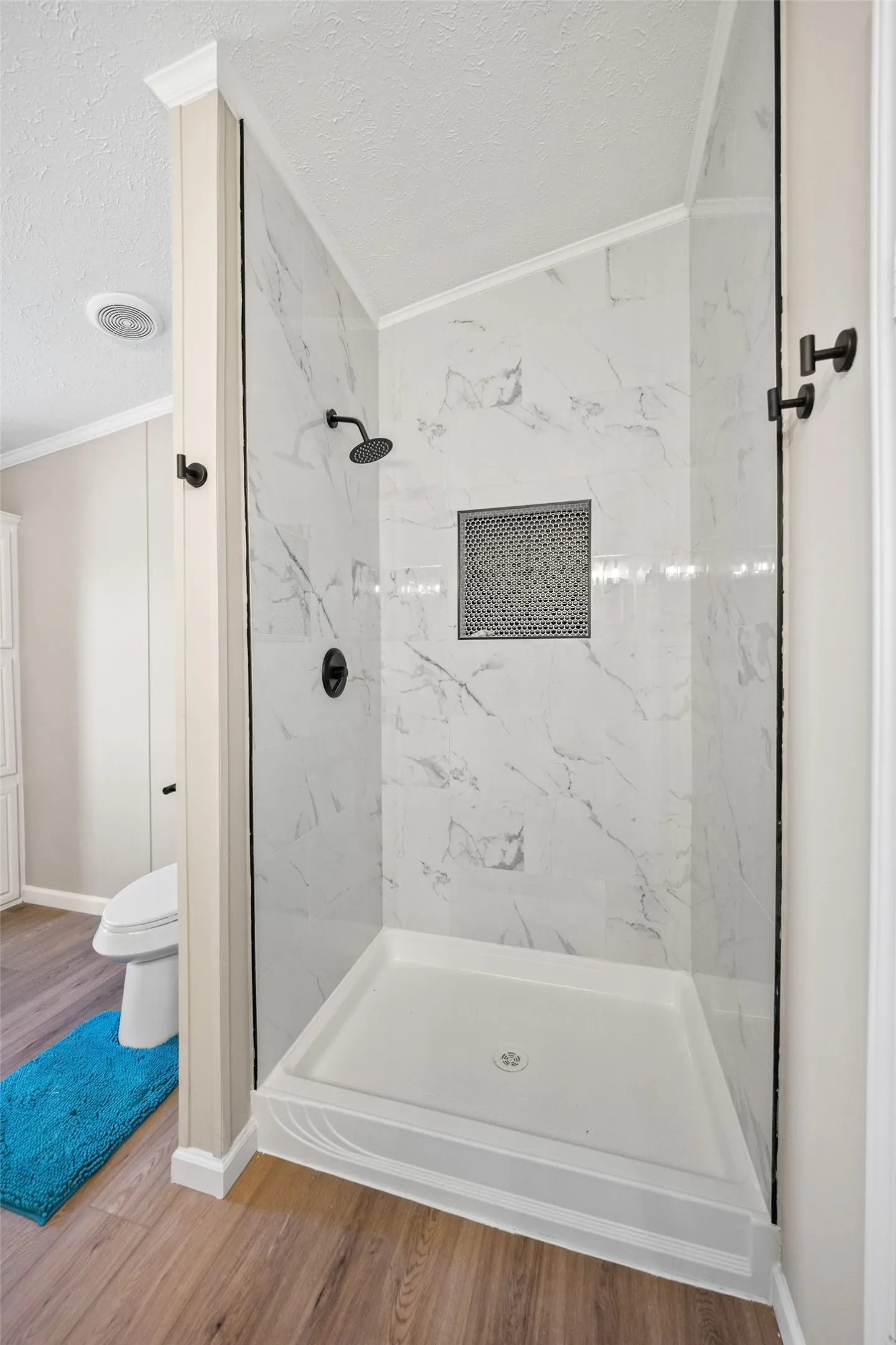 Walk-in shower with white marbled tile surround, black shower fixtures, and a built-in shower niche