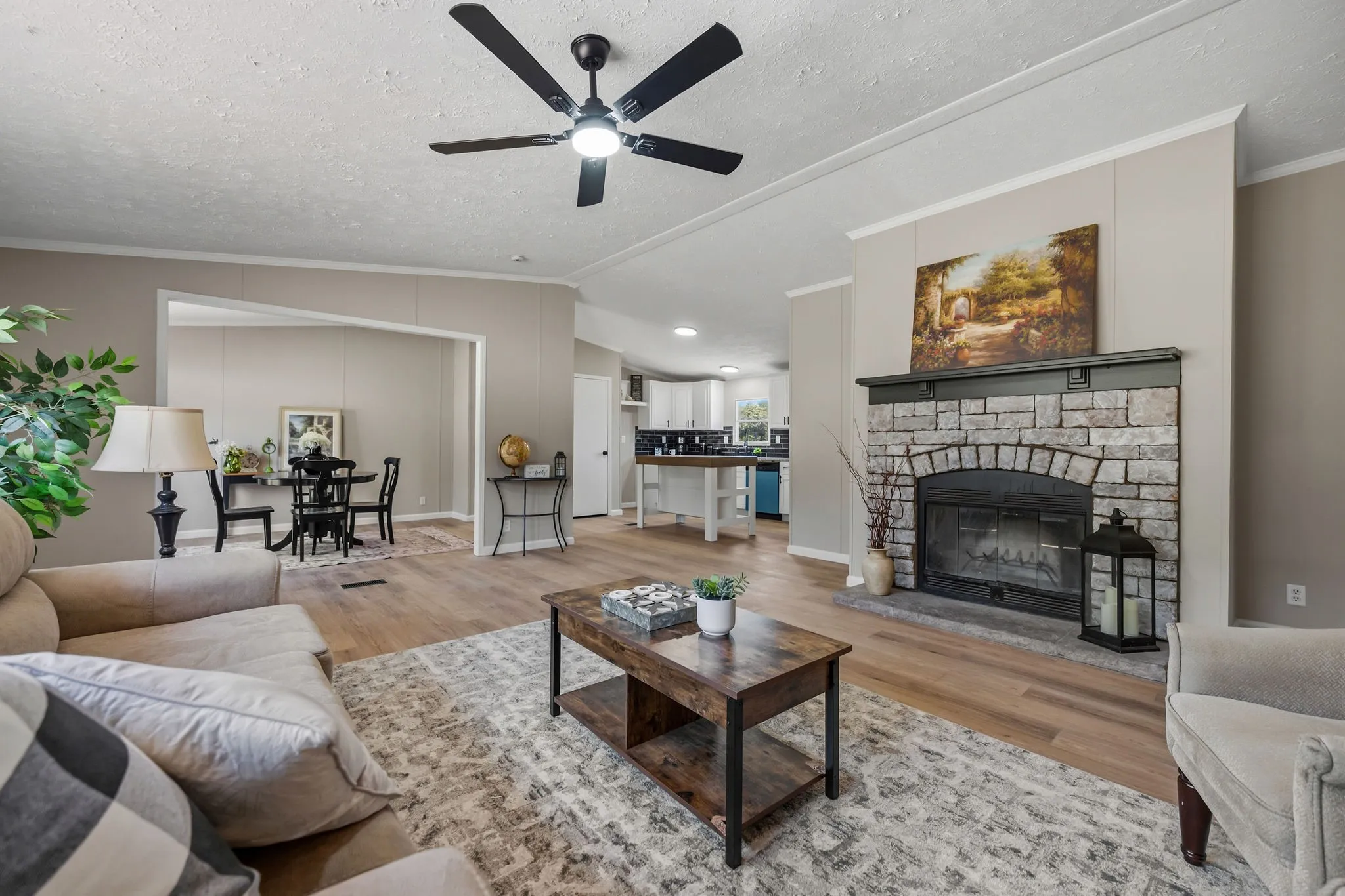 Spacious living area featuring wood-finish flooring, a stone-faced fireplace with a dark mantel, and an overhead ceiling fan