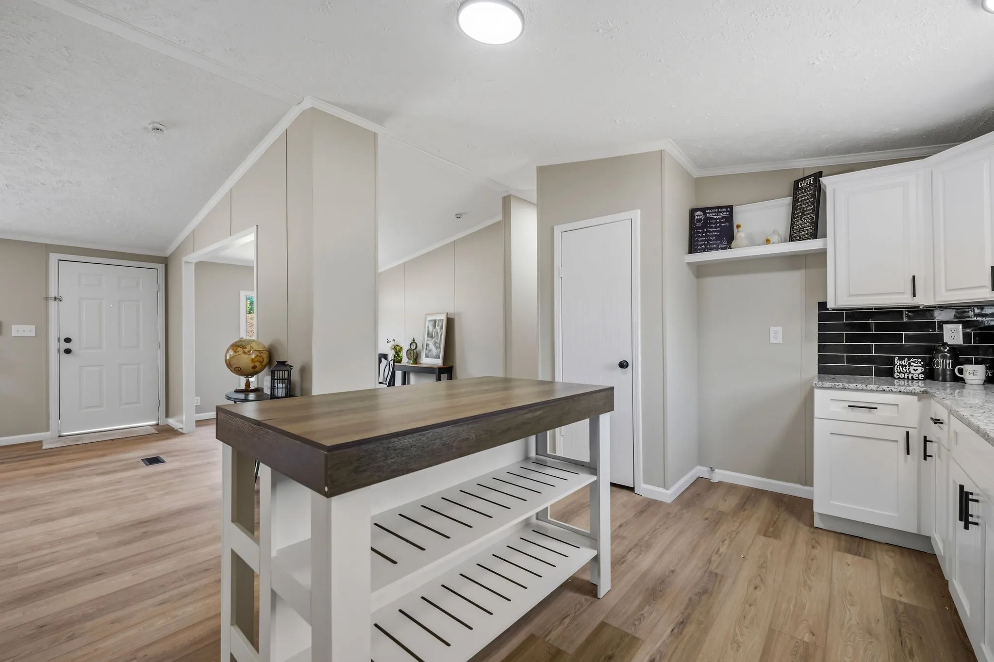 Kitchen featuring wood-finish flooring, white cabinetry with black hardware, a black subway tile backsplash, and light-toned countertops