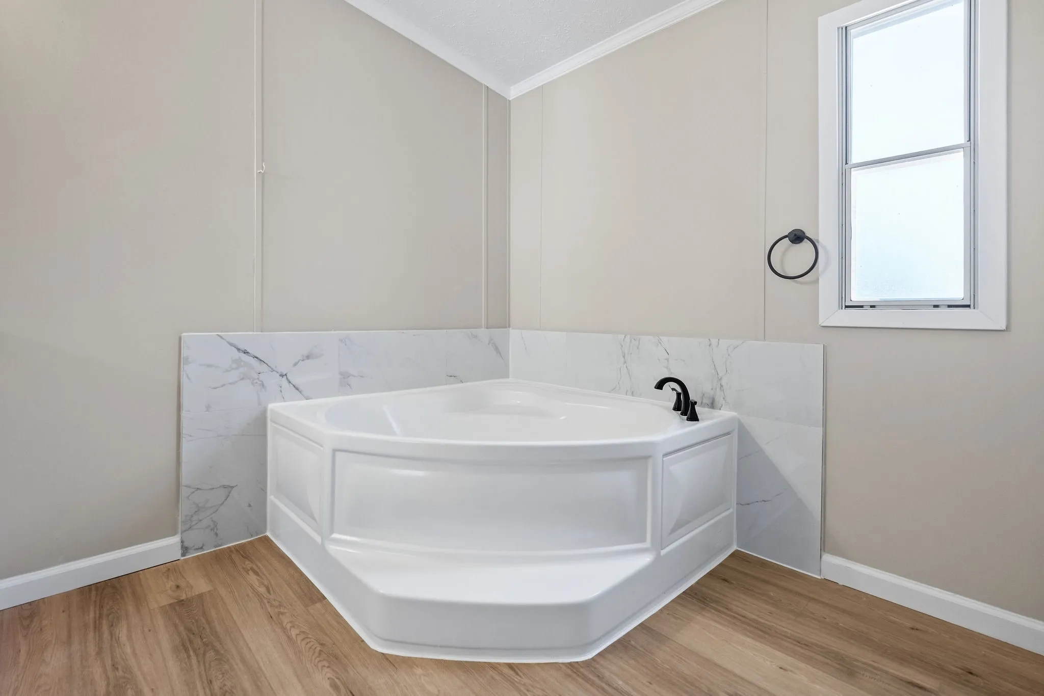 Corner soaking tub with built-in steps, wood-finish flooring, and a white framed window