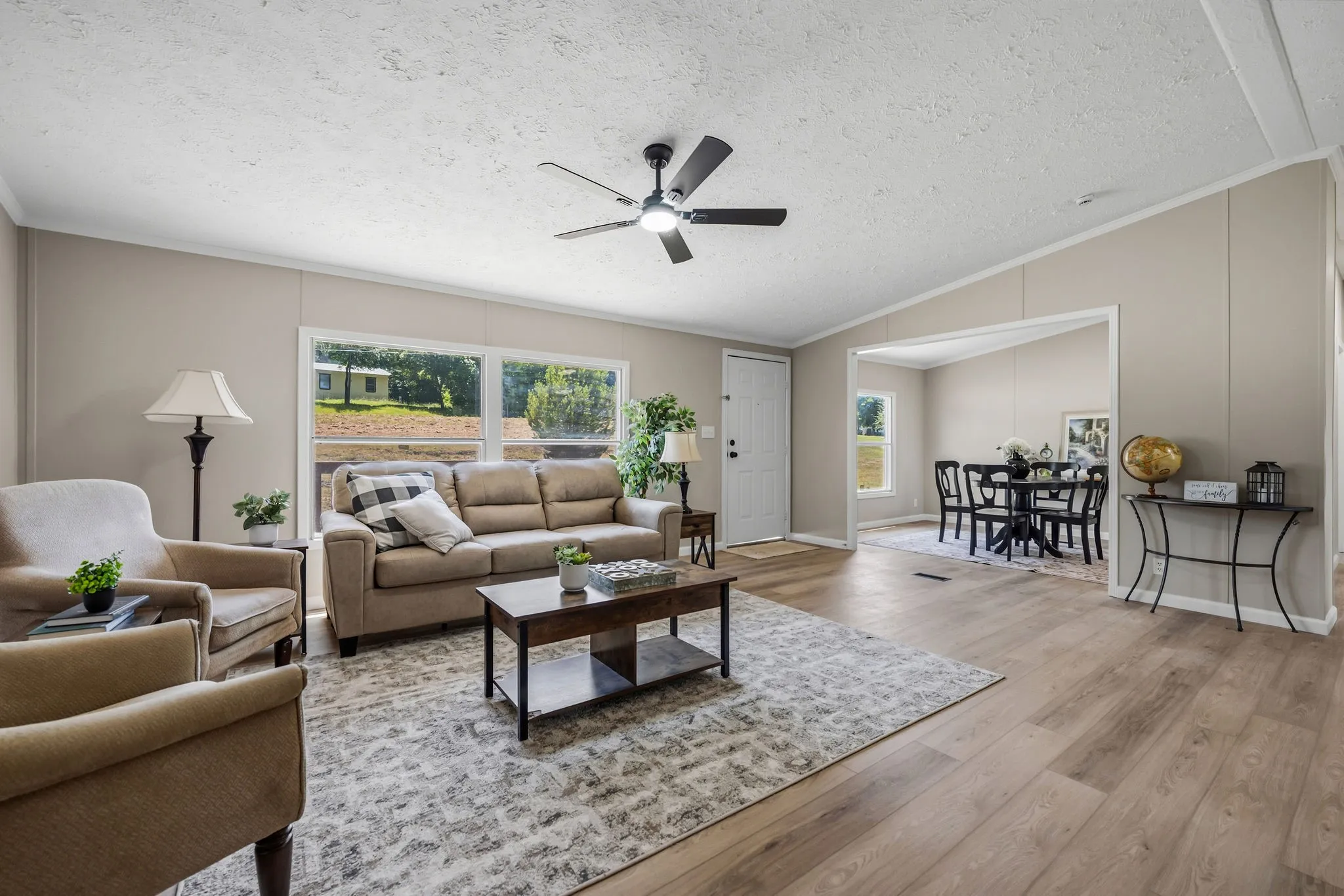 Open-concept living area featuring wood-finish flooring, a ceiling fan, and large windows