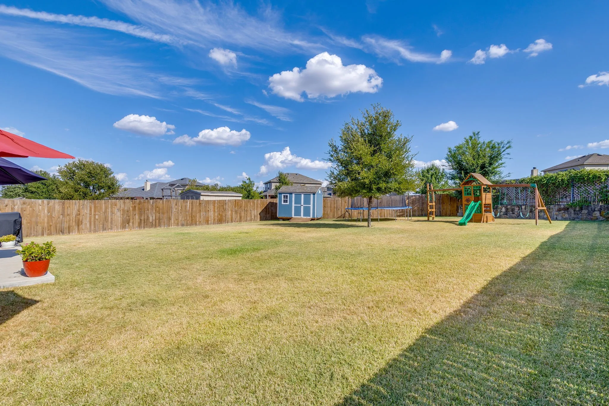 Expansive backyard featuring a manicured lawn, wood privacy fencing, a storage shed, and mature trees