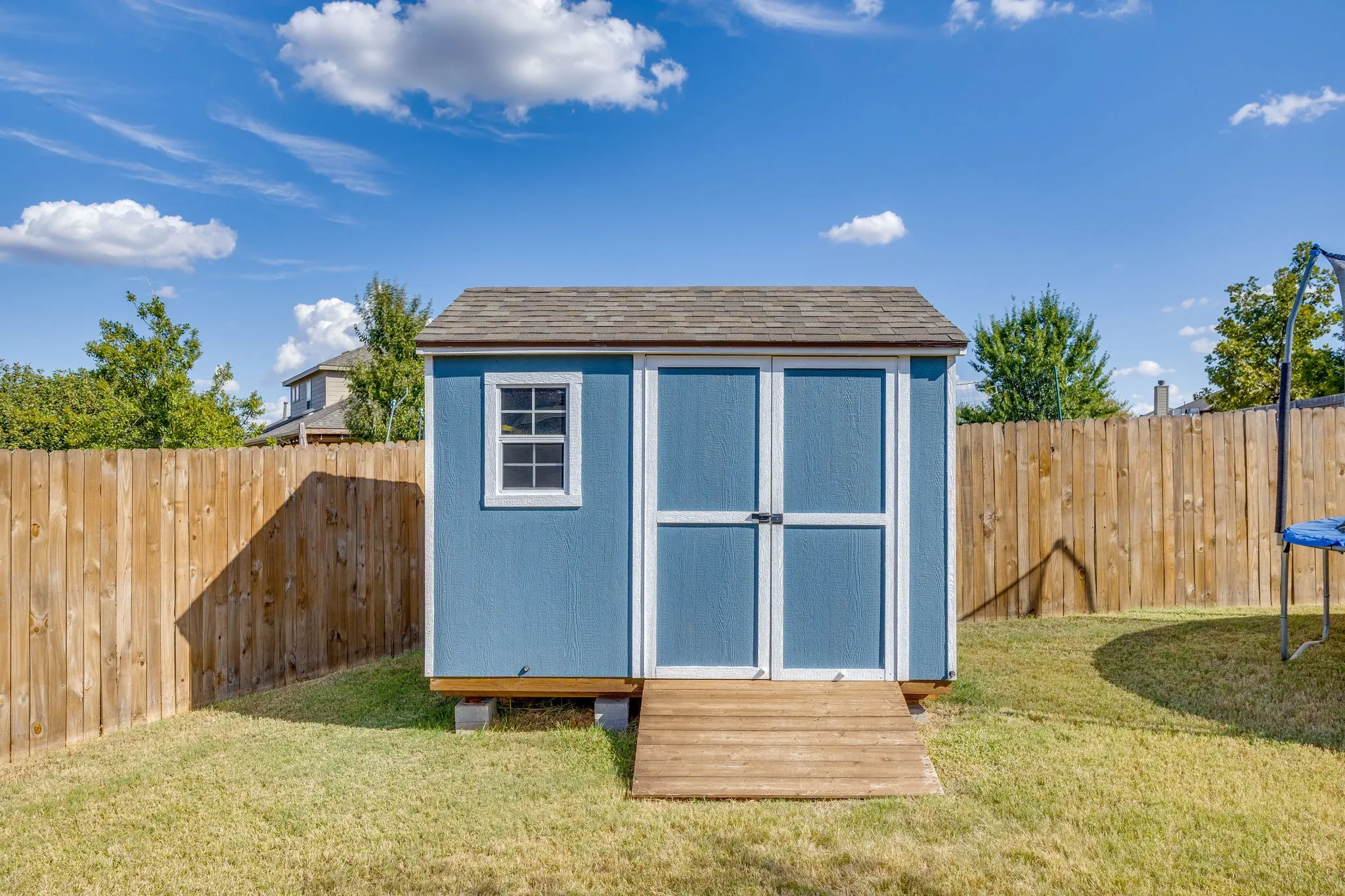 Grassed backyard featuring a blue storage shed with a shingle roof, double doors, a single window, and a wood ramp