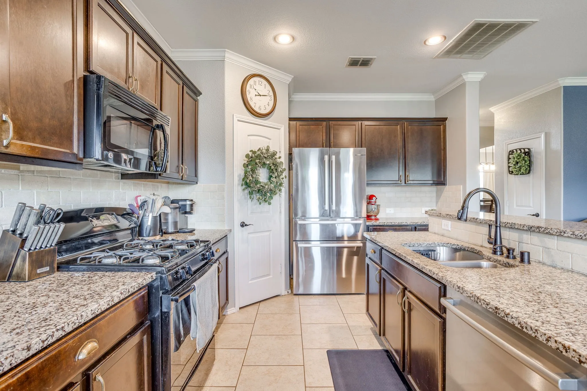 Kitchen featuring stainless steel appliances, granite countertops, tile flooring, rich wood cabinetry, and a tile backsplash