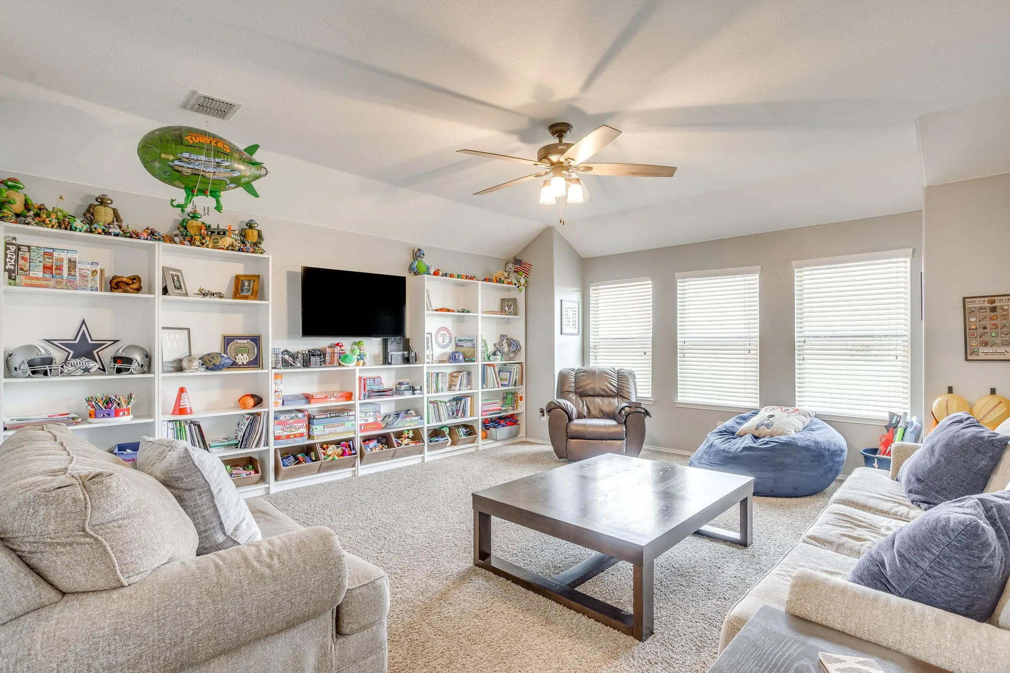 Vaulted ceiling with a ceiling fan, multiple windows with blinds, built-in shelving, and carpet flooring
