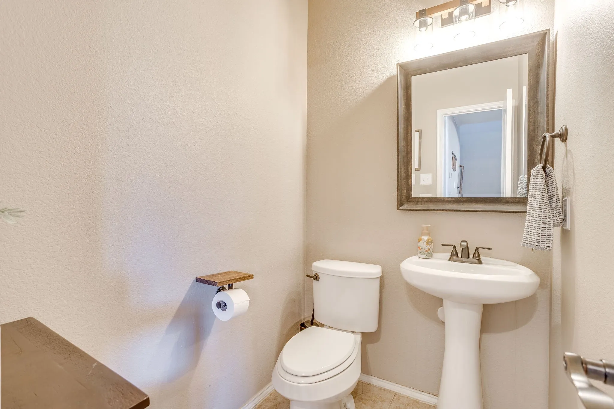 Pedestal sink, wall-mounted mirror with wood-finish frame, and overhead vanity lighting