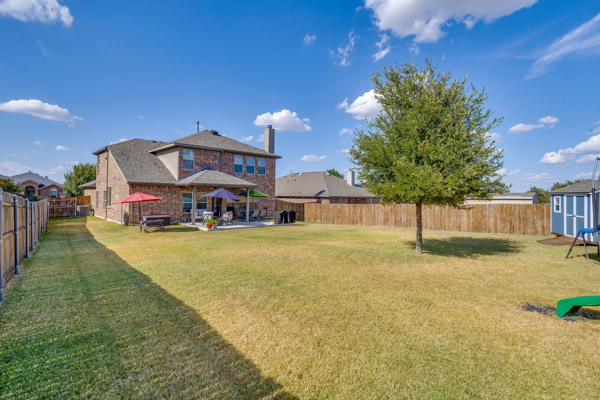 Expansive backyard featuring a mature tree, privacy fencing, and a covered patio