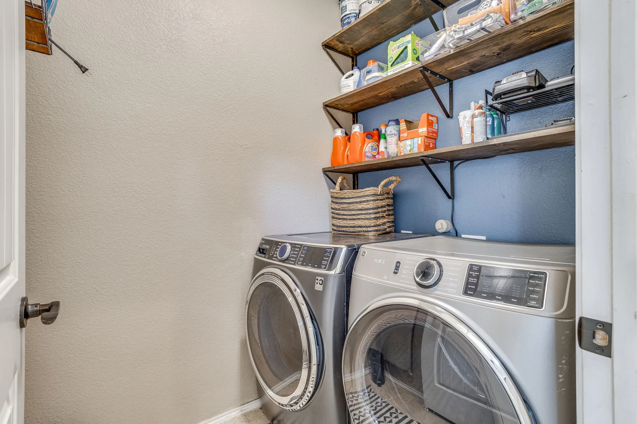 Laundry area featuring permanent shelving, a blue accent wall, and a textured wall finish
