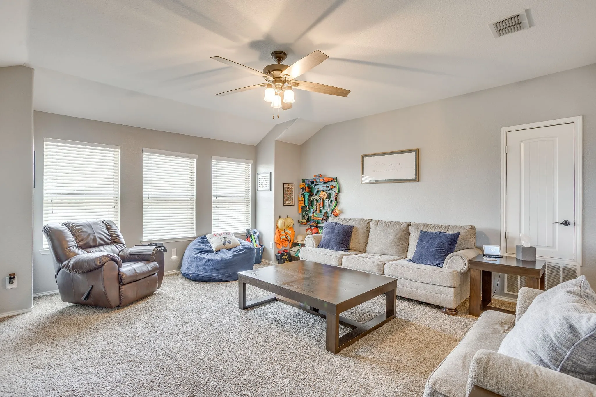 Carpeted flooring, vaulted ceiling, ceiling fan with integrated lighting, multiple windows with blinds, and a paneled door