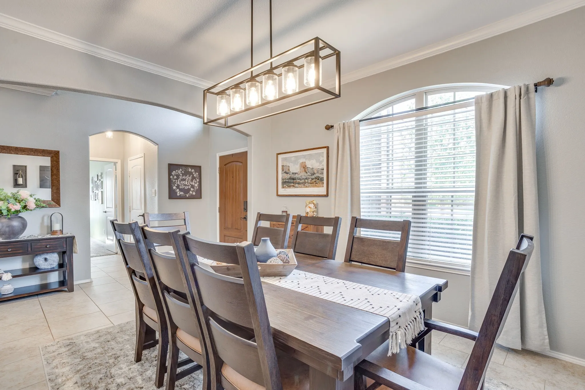 Arched window with blinds, tile flooring, crown molding, and an arched doorway