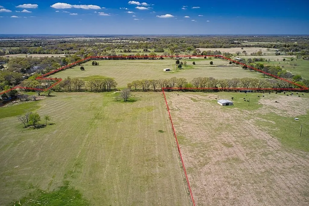 Expansive agricultural land featuring a clear-span metal building, mature trees, and a visible property boundary