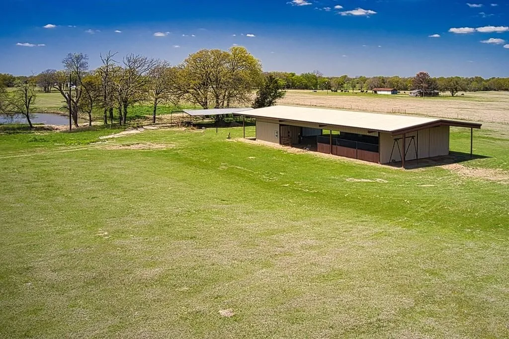 Expansive green pasture with a rectangular outbuilding featuring a shed roof, enclosed stalls, and an open-air extension