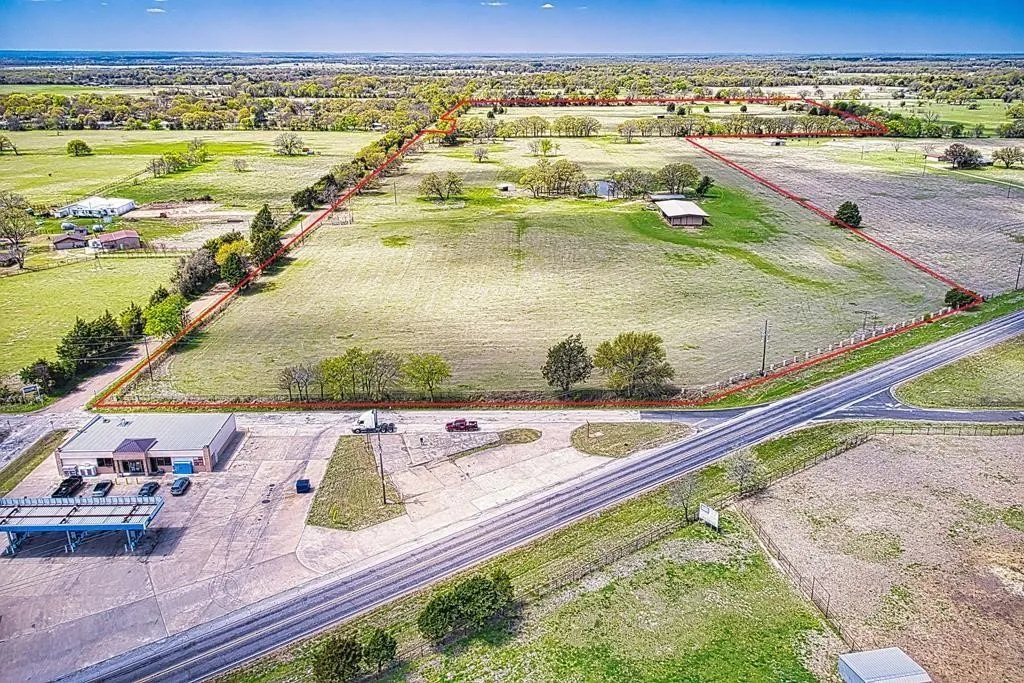 Expansive acreage with a single-story commercial building, mature trees, and a paved road frontage