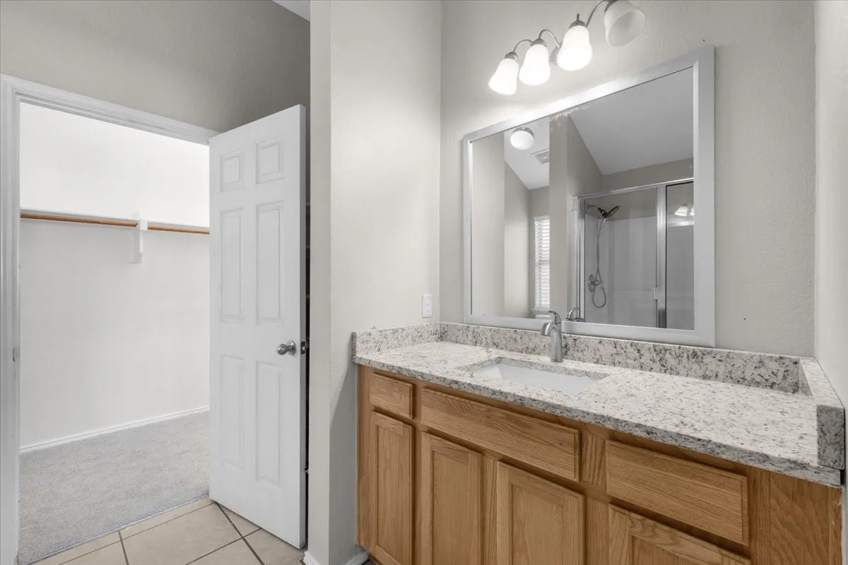 Vanity with light wood-finish cabinetry, light speckled countertop, and undermount sink