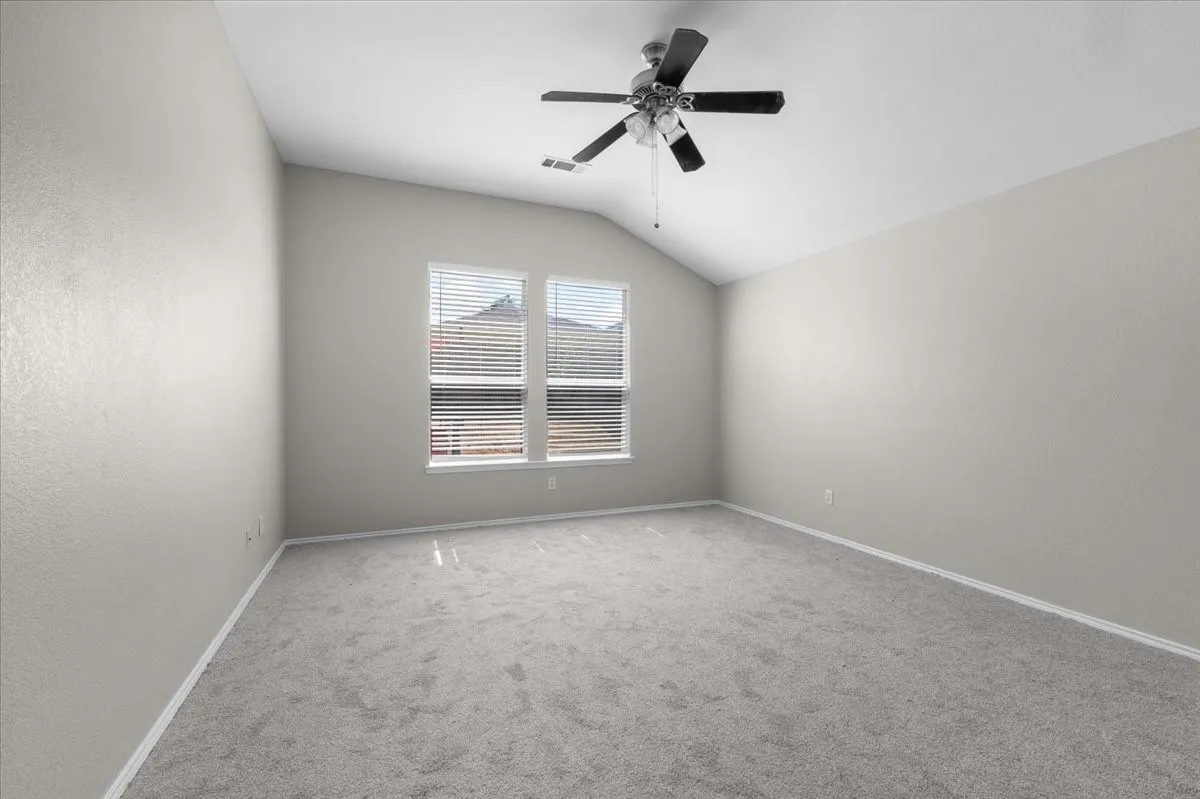 Vaulted ceiling, ceiling fan with integrated lighting, dual windows with blinds, light-toned carpeting, and painted walls