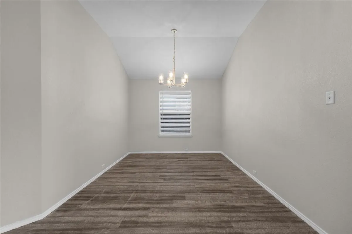 Window with blinds, wood-finish flooring, and a decorative chandelier
