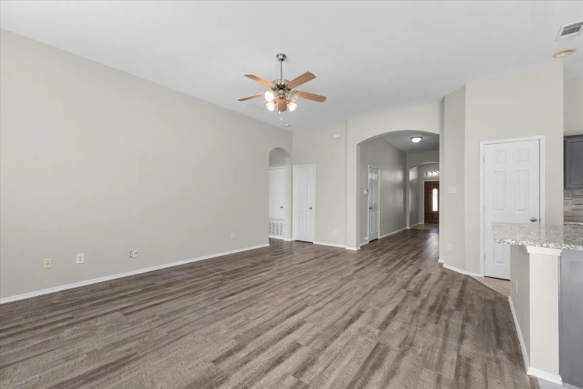 Wood-finish flooring throughout, neutral wall tones, arched doorways, and a ceiling fan with integrated lighting
