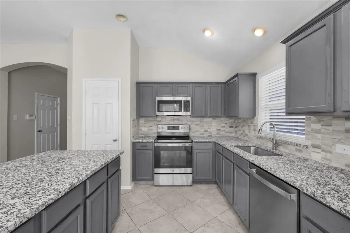 Kitchen featuring gray cabinetry, light-toned granite countertops, stainless steel appliances, and a mosaic tile backsplash
