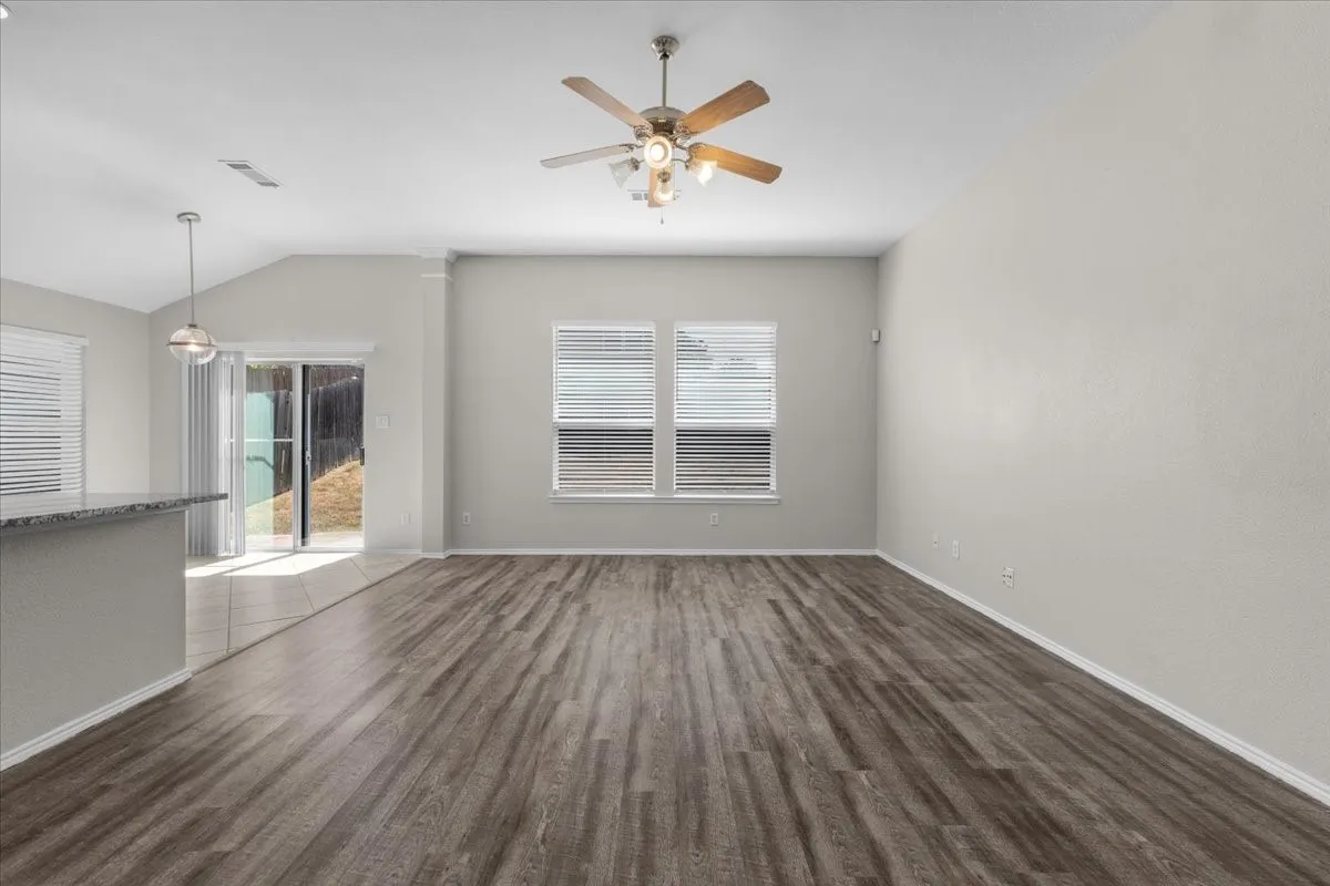 Wood-finish flooring throughout, vaulted ceiling, ceiling fan with integrated lighting, multiple windows with blinds, and a sliding glass door
