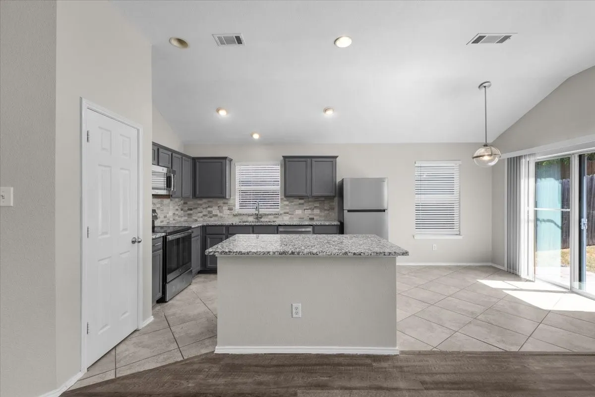 Kitchen featuring dark cabinetry, stainless steel appliances, a center island with a speckled countertop, and a tile backsplash