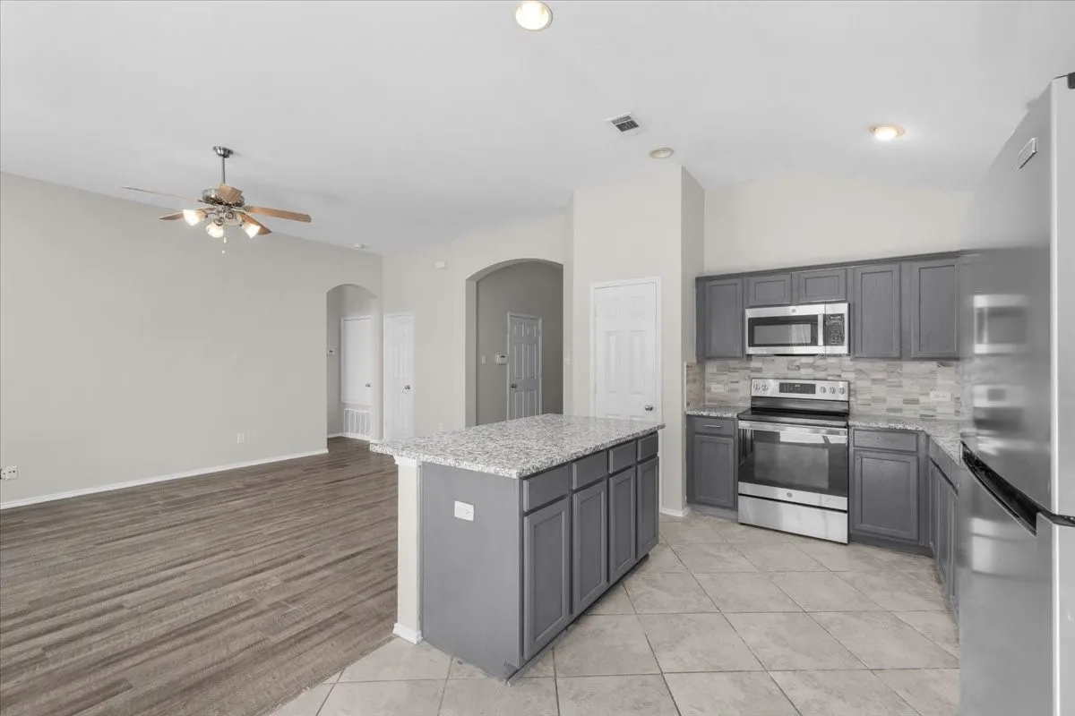 Kitchen island with granite countertop, gray cabinetry, and stainless steel appliances
