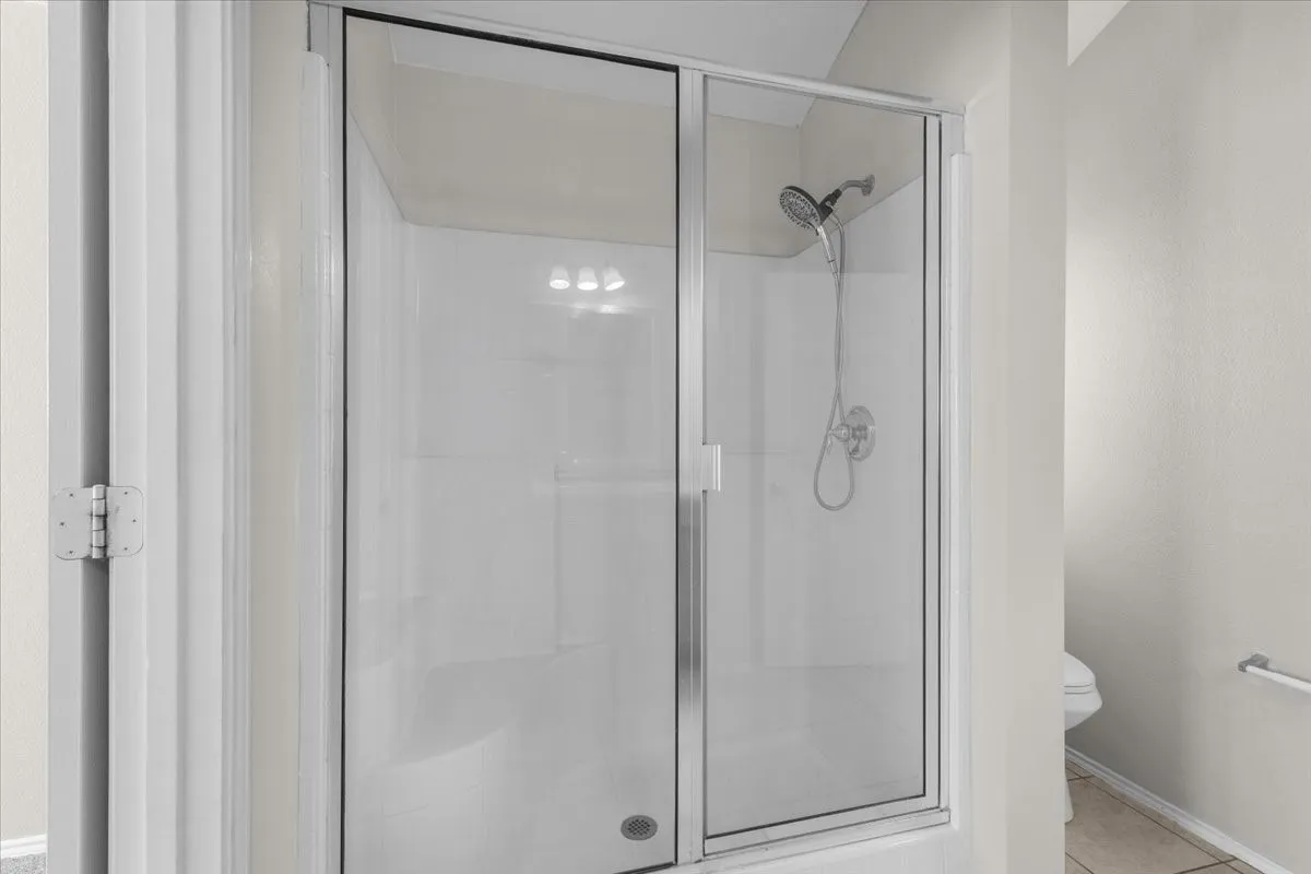 Glass-enclosed shower with a multi-function showerhead, integrated shower caddy, and overhead lighting
