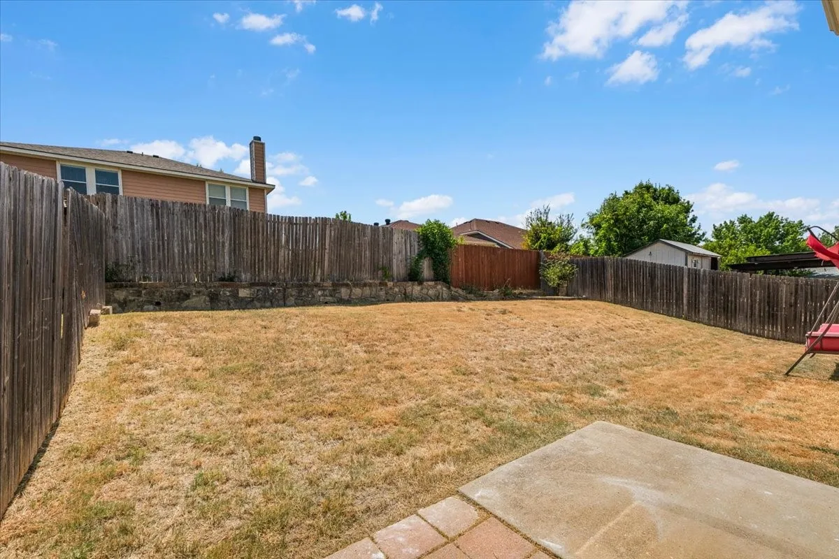 Expansive backyard featuring a privacy fence, concrete patio, and a stone retaining wall