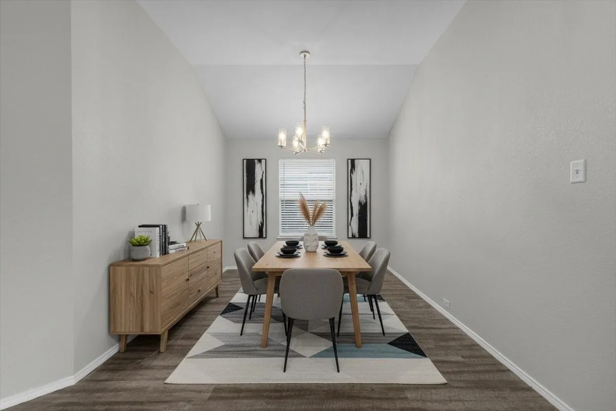 Vaulted ceiling accentuates the formal dining space, featuring wood-finish flooring and a central chandelier (virtually staged)