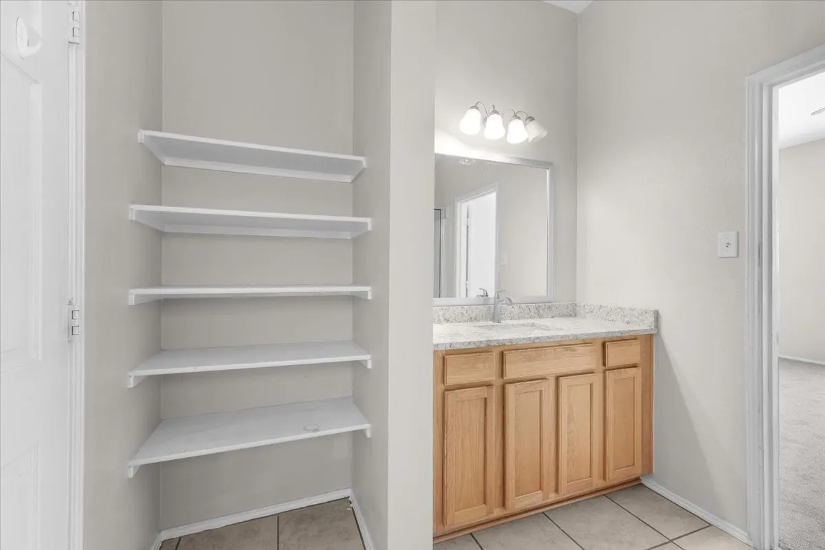 Built-in shelving unit, wood-finish vanity, light-toned countertop, rectangular sink, and tile flooring