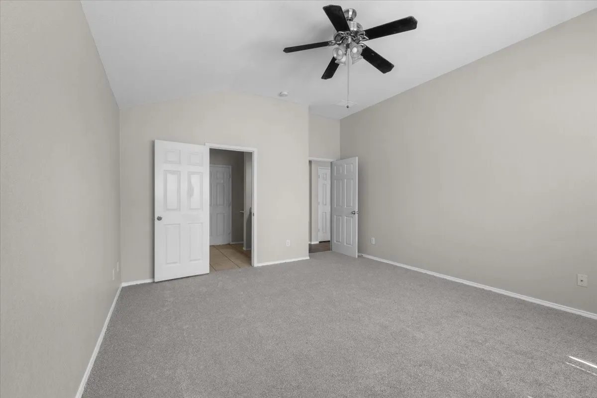 Vaulted ceiling with a ceiling fan, light gray wall paint, and gray carpeting